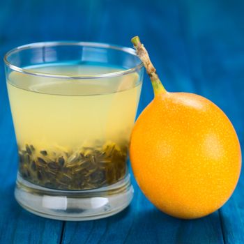 Fresh juice made of sweet granadilla or grenadia (lat. Passiflora ligularis) with its seeds in glass, granadilla fruit on the side (Selective Focus, Focus on the front rim of the glass and on the front of the granadilla)