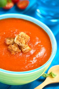 Fresh homemade tomato soup with wholegrain croutons on top served in colorful bowl on blue wood (Selective Focus, Focus on the croutons in the front) 