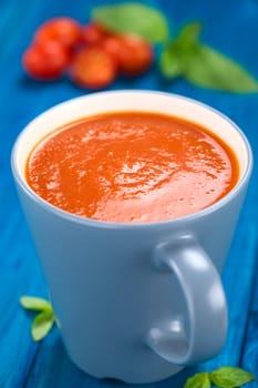 Fresh homemade tomato soup served in blue cup on blue wood (Selective Focus, Focus one third into the soup) 