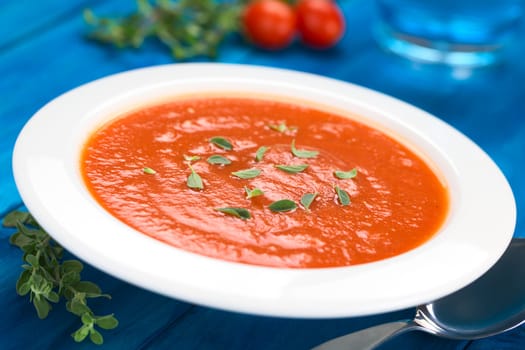 Fresh homemade tomato soup with oregano leaves on top served in soup plate on blue wood (Selective Focus, Focus one third into the soup) 