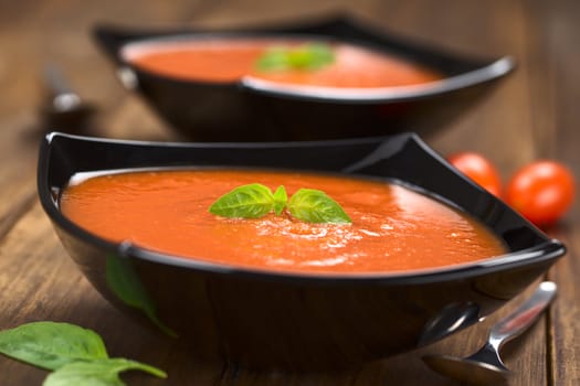 Fresh homemade tomato soup with basil leaf on top served in black bowl on dark wood (Selective Focus, Focus on the basil leaf on the tomato soup) 