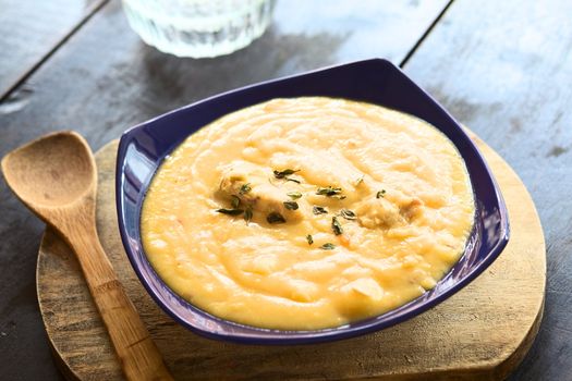 Thick yellow split pea soup with chicken and some oregano leaves on top served in blue soup plate on wooden board (Selective Focus, Focus in the middle of the soup)