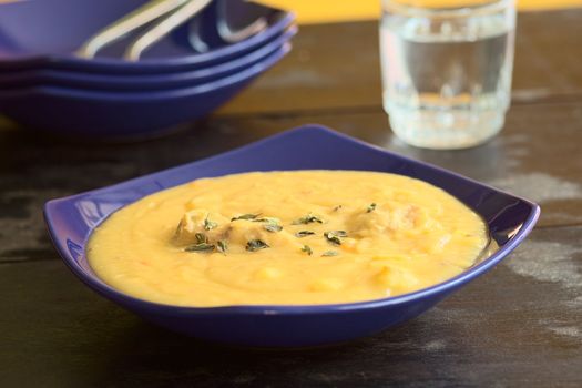 Thick yellow split pea soup with chicken and some oregano leaves on top served in blue soup plate (Selective Focus, Focus one third into the soup)