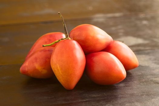 Pile of tamarillo fruits (lat. Solanum betaceum) on dark wood. In Ecuador, tamarillo is blended with water or milk and sugar to make a refreshing drink. (Selective Focus, Focus on the first two tamarillos)