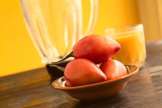 Tamarillo fruits (lat. Solanum betaceum) in bowl with tamarillo juice and blender in the back. In Ecuador, tamarillo is blended with water or milk and sugar to make a refreshing drink. (Selective Focus, Focus on the upper tamarillo)