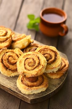 Freshly prepared homemade cinnamon rolls on wooden board with tea in cup in the back (Selective Focus, Focus on the middle of the top cinnamon roll)