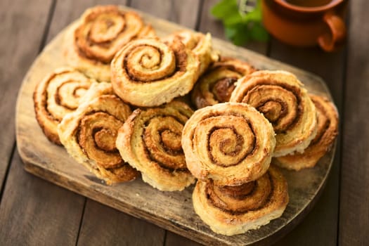 Freshly prepared homemade cinnamon rolls on wooden board with tea in cup in the back (Selective Focus, Focus on the middle of the top cinnamon roll)