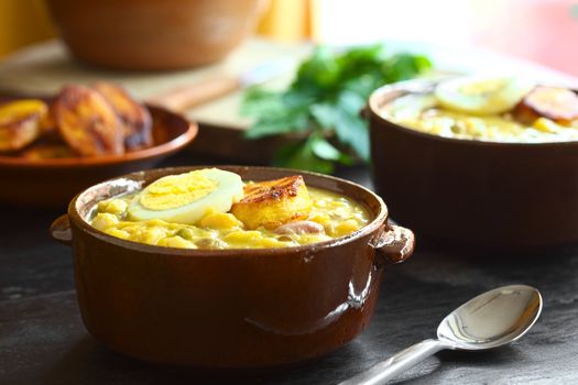 Ecuadorian soup called Fanesca, which is traditionally eaten at Easter and is prepared from many different legumes (such as lentils, beans, kidney beans, dried green peas, fava beans, chickpeas, lupines, etc), gourd, pumpkin, milk and salt cod and is usually served with fried plantain, boiled eggs and cheese (Selective Focus, Focus on the front of the egg slice and fried plantain on top of the meal) 