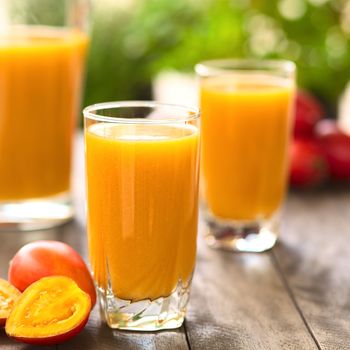 Fresh juice out of tamarillo fruits (lat. Solanum betaceum) on a table outdoors (Selective Focus, Focus on the front rim of the glass)