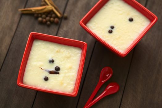 Two red bowls of the Ecuadorian dessert called morocho (coarsely ground white corn) cooked with milk, sugar and spices (cinnamon and allspice), similarly to rice pudding (Selective Focus, Focus on the cinnamon stick in the lower bowl) 