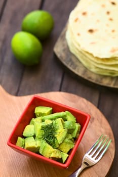 Fresh avocado salad prepared with lime juice, pepper, salt and garnished with fresh coriander leaves, homemade tortillas in the back (Selective Focus, Focus in the middle of the salad)  