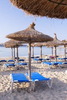 Beautiful Sandy Beach with Straw Umbrellas at Sunrise in Paguera, Majorca ( Balearic Islands - Spain )