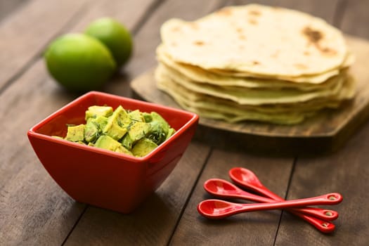 Fresh avocado salad prepared with lime juice, pepper, salt and sprinkled with fresh coriander leaves, homemade tortillas in the back (Selective Focus, Focus in the middle of the salad)  