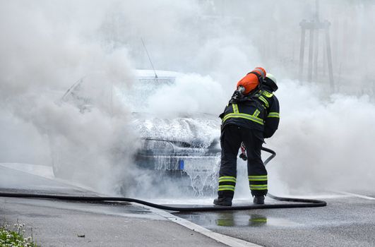 Burning motor vehicle been put out by fireman in protective clothing