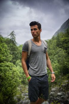 Handsome muscular young man backpacking or hiking in lush green mountain scenery pausing to look at something  far away