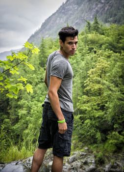 Handsome muscular young man hiking in lush green mountain scenery looking at camera