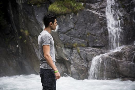 Handsome young man looking at mountain waterfall, profile view.