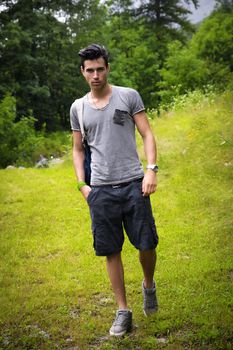 Handsome muscular young man backpacking or hiking in lush green mountain scenery looking at camera