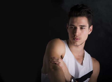 Handsome black haired young man on dark background, looking to a side