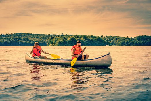 Men sailing a canoe wearing orange lifejackets