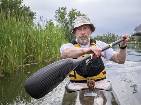 senior male paddler training in a narrow fast racing kayak on a lake in Colorado