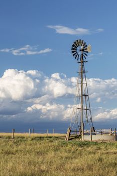 windmill with a pump and cattle water tank in shortgrass prairie against stormy sky, Pawnee National Grassland in Colorado near Grover