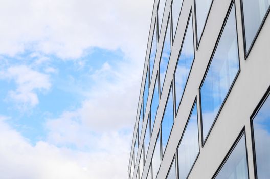 Blue sky and clouds reflected in mirrored windows of new modern building glass facade. Background with free copy-space area for your text.