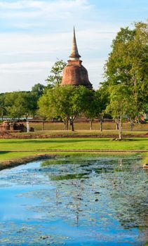 Ruins of Buddhist stupa or chedi in Sukhothai historical park in Wat Chana Songkhram temple with water pond lake on front. 