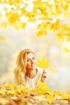 Young woman laying down on the ground covered dry autumnal foliage in beautiful park