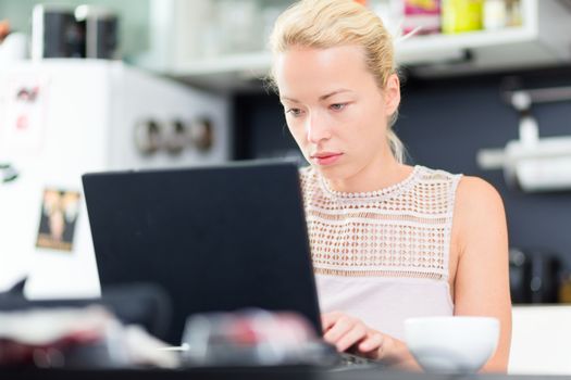Business woman working remotly from her dining table. Home kitchen in the background.