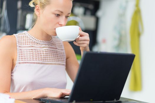Business woman working remotly from her dining table while having her morning coffee. Home kitchen in the background.