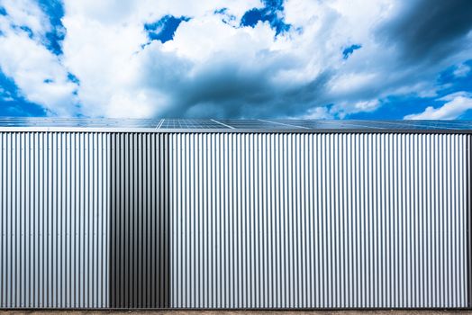 exterior of a modern commercial warehouse with solar panels on the roof against great cloudy sky