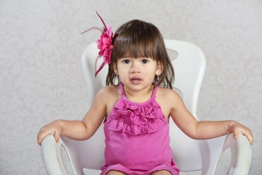 Cute toddler in chair with pink ribbon in hair