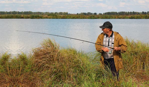 old fisherman with spinning rod on lake