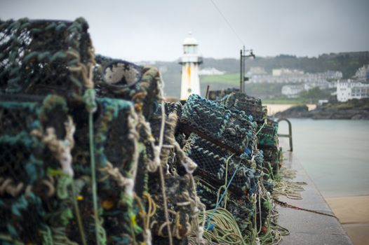 Fishing at St Ives harbor with a view past a stack of old wire lobster or crab traps to the lighthouse at the harbor entrance