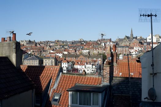View over rooftops of a town with historical buildings and chimney pots and a distant church on a hill