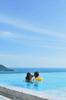 Summer vacations concept. Happy mother and daughter playing in blue water of swimming pool.