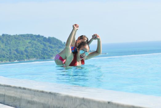 Summer vacations concept. Happy mother and daughter playing in blue water of swimming pool.