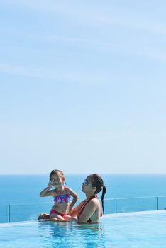 Summer vacations concept. Happy mother and daughter playing in blue water of swimming pool.