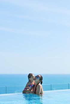 Summer vacations concept. Happy mother and daughter playing in blue water of swimming pool.