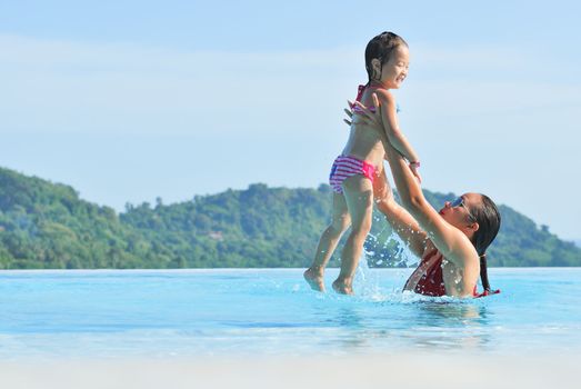 Summer vacations concept. Happy mother and daughter playing in blue water of swimming pool.