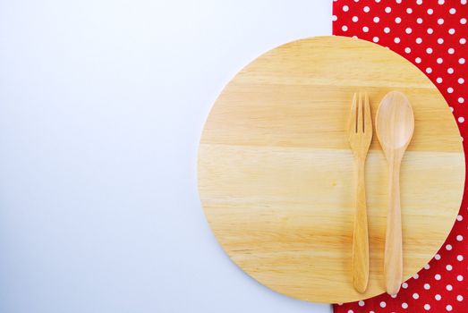 Wooden plate, tablecloth, spoon, fork on table background