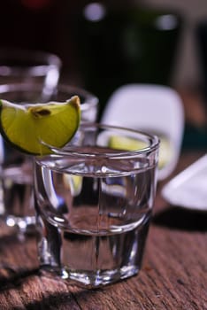 Glass of vodka shot with fresh lime on wooden table