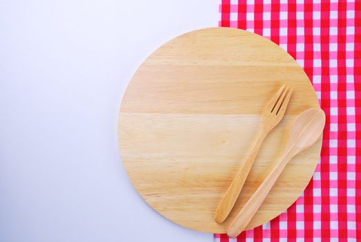 Wooden plate, tablecloth, spoon, fork on table background