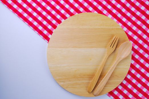 Wooden plate, tablecloth, spoon, fork on table background
