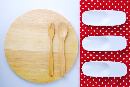 Wooden plate, tablecloth, spoon, fork on table background