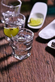 Glass of vodka shot with fresh lime on wooden table