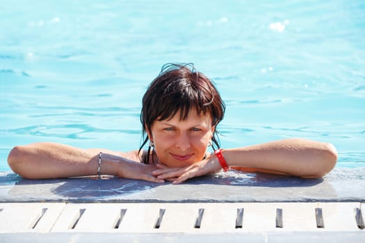 smiling middle age woman relaxing in swimming pool on resort