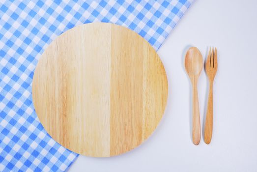 Wooden plate, tablecloth, spoon, fork on table background