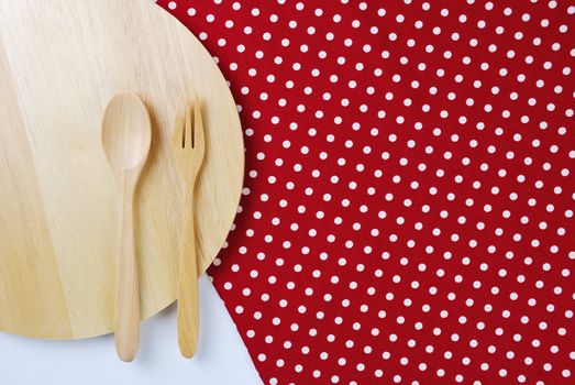 Wooden plate, tablecloth, spoon, fork on table background